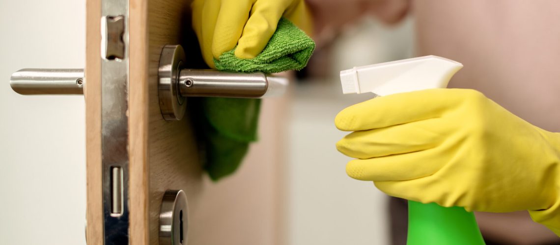 Close-up of woman cleaning door handle with disinfectant.